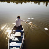 Mann in einem Boot fischt Papiere aus dem Wasser.
