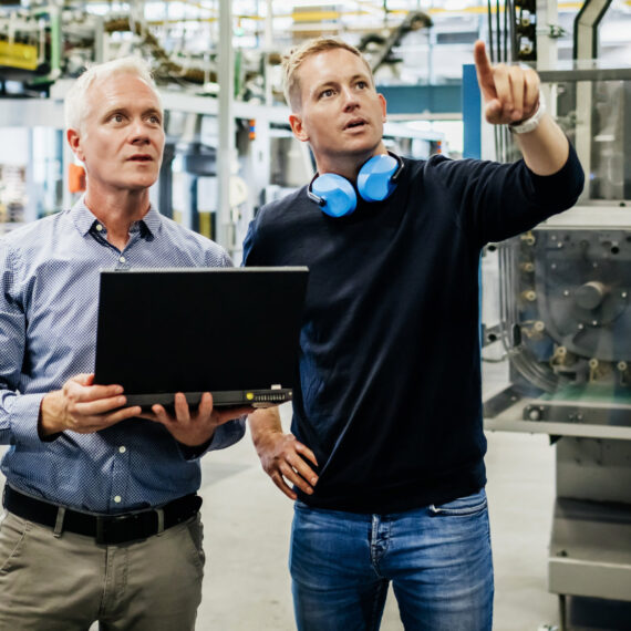 Servitization, die Zukunft im Manufacturing (zwei Männer zeigen etwas in einer Fabrik)